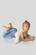 Child wearing blue cotton pants and a red polka dot open back top lying on a light grey surface
