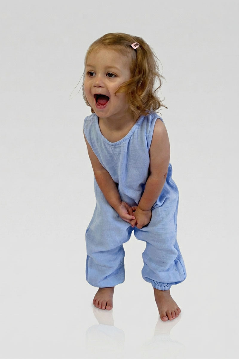 Child wearing a light blue sleeveless jumpsuit and laughing on a white background