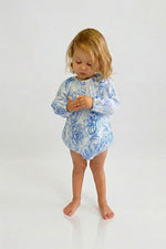 Child wearing a blue paisley romper on a white background