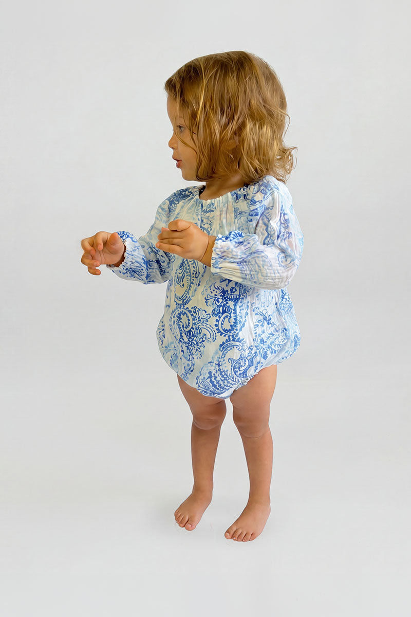 Child wearing a blue paisley romper with long sleeves on a plain background