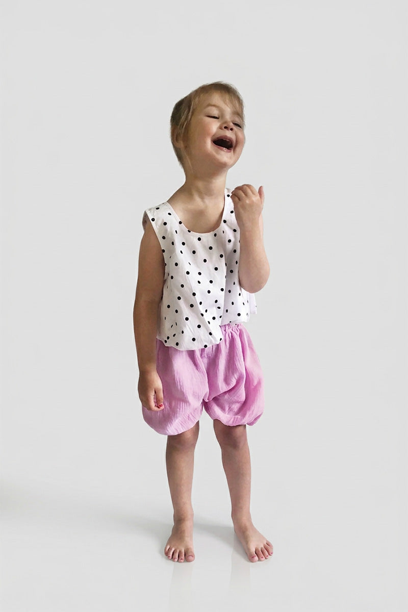 Child wearing pink bubble shorts with a polka dot top on a white background