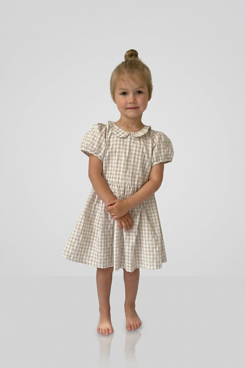 Young girl wearing a Gingham Caramel dress on a plain background