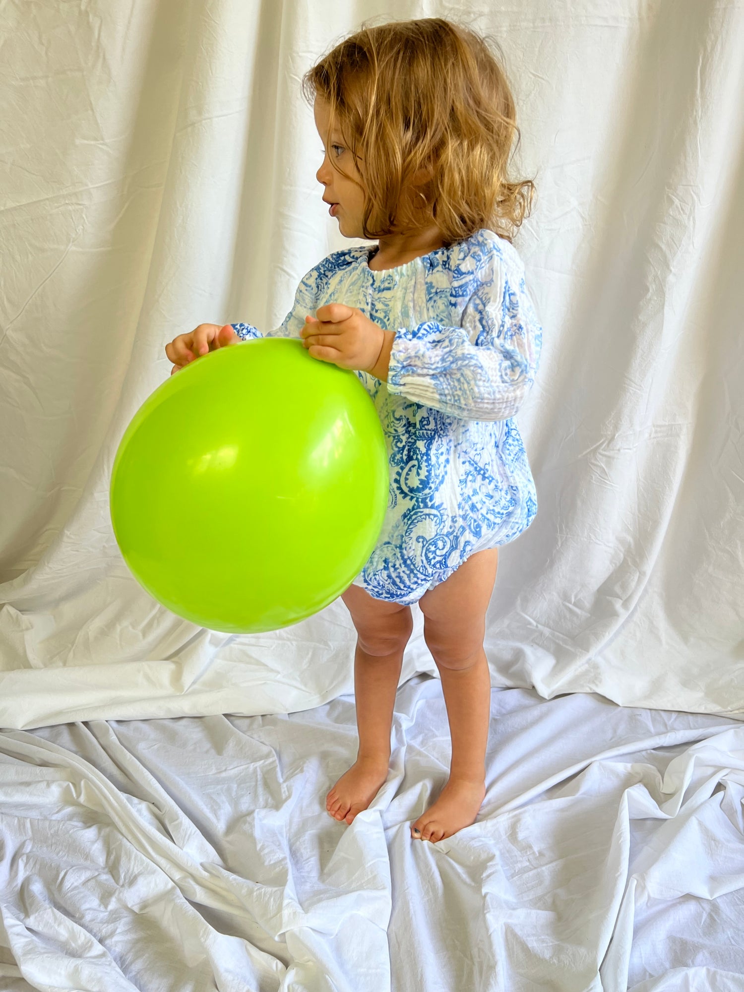 Young child holding a balloon wearing a Long Sleeve Romper in Blue Paisley colour