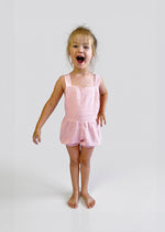 Child wearing a light pink bubble overalls on a plain background