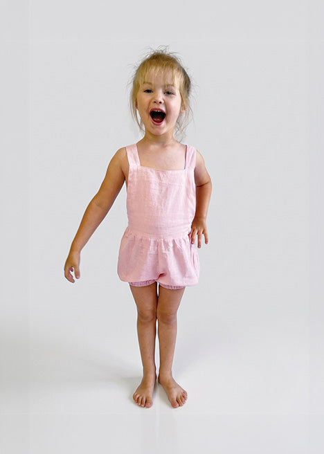 Child wearing a light pink bubble overalls on a plain background