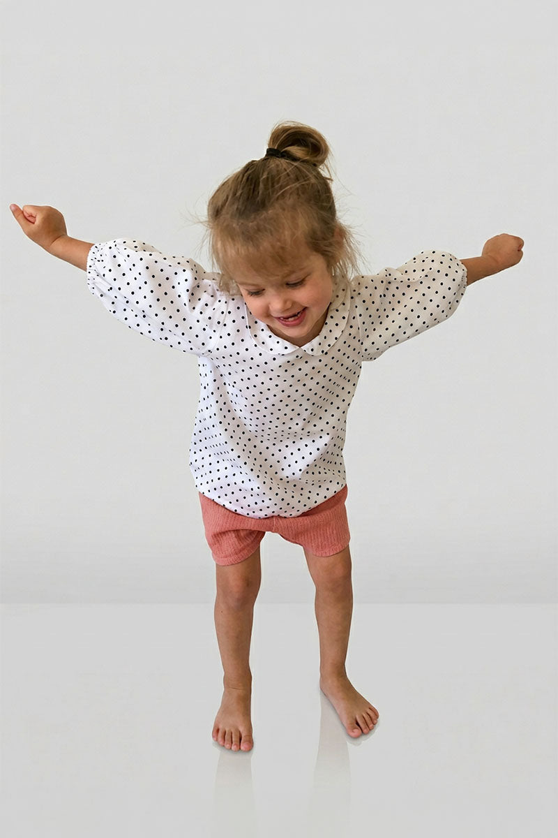 Child wearing a polka dot bubble sleeve blouse and pink shorts on a white background