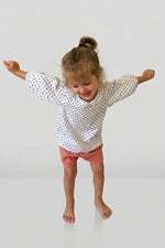 Child wearing a polka dot bubble sleeve blouse and pink shorts on a white background