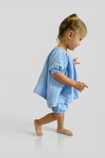 Young girl wearing a blue short sleeve puff top and matching blue bloomers on a plain background