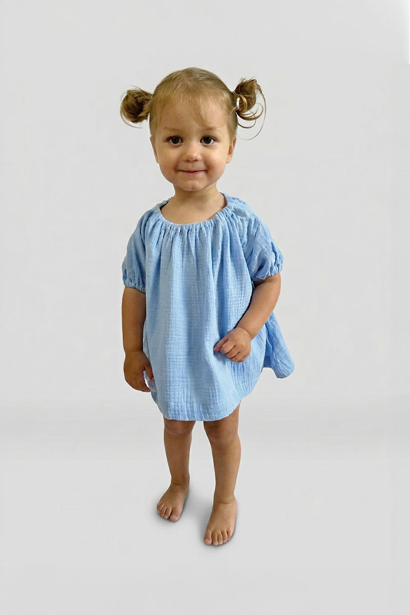 Young girl wearing a blue short sleeve puff top and matching blue bloomers on a plain background