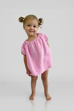 Young girl wearing a pink short sleeve puff top and matching pink bloomers on a plain background