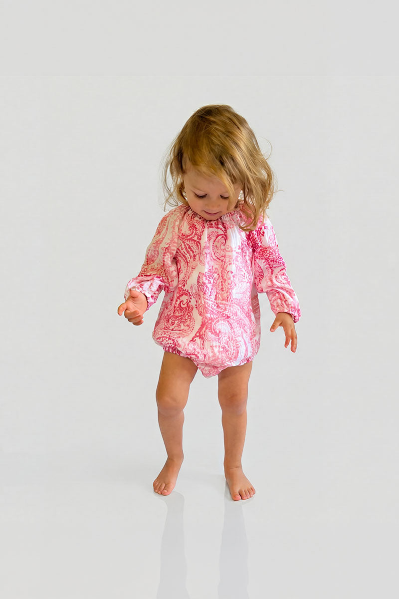 Child wearing a Red Paisley Romper with long sleeves looking down on a white background