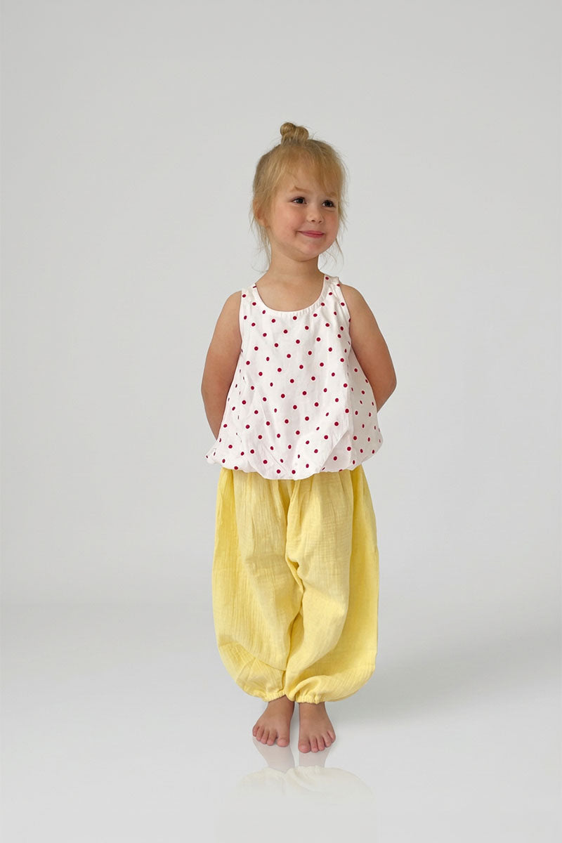 Child wearing a Red Polka Dot open back top and yellow pants on a white background