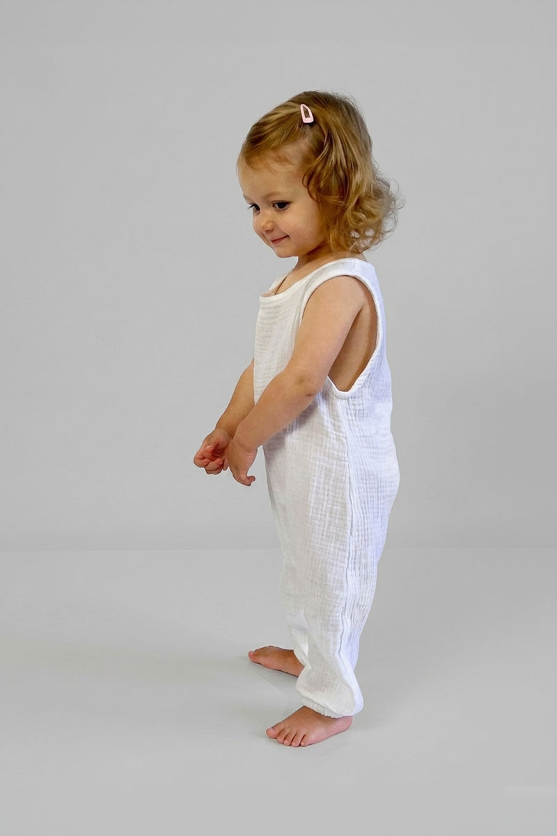 Young child wearing a white sleeveless jumpsuit on a plain background