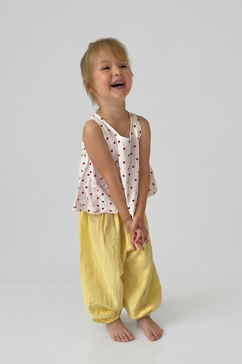 Child wearing yellow pants with red polka dot top on a plain background
