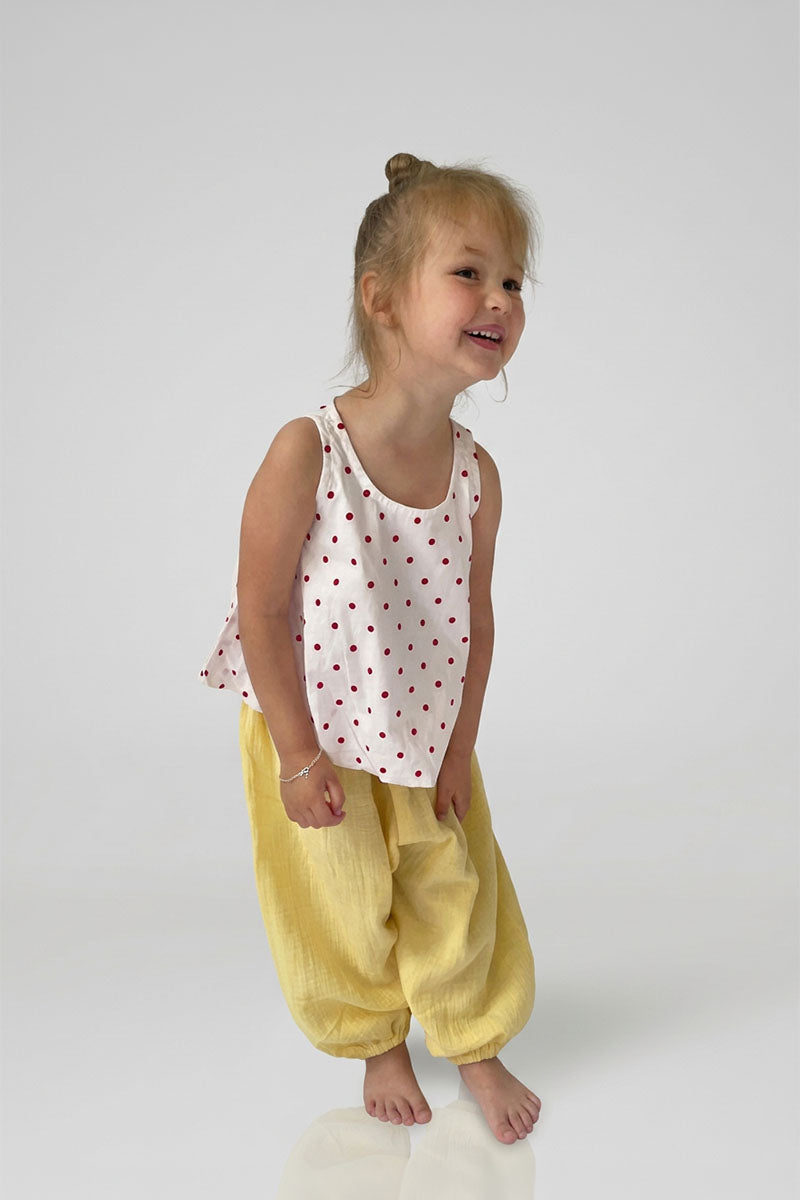 Child wearing yellow pants with red polka dot top on a plain background