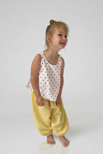 Child wearing yellow pants with red polka dot top on a plain background