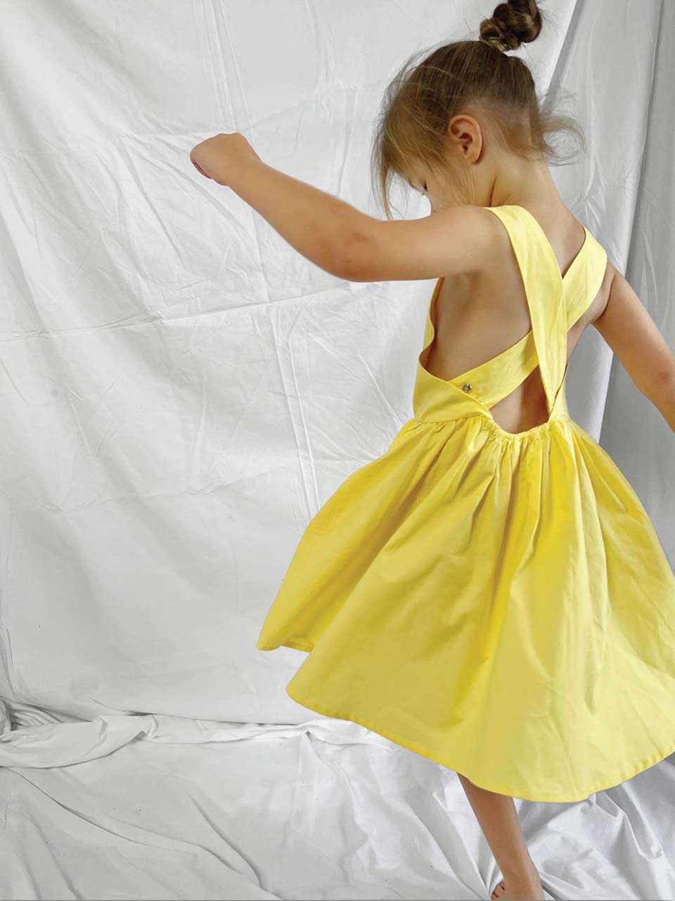 Side and back shot of a yellow pinafore dress worn by a young girl with a white background