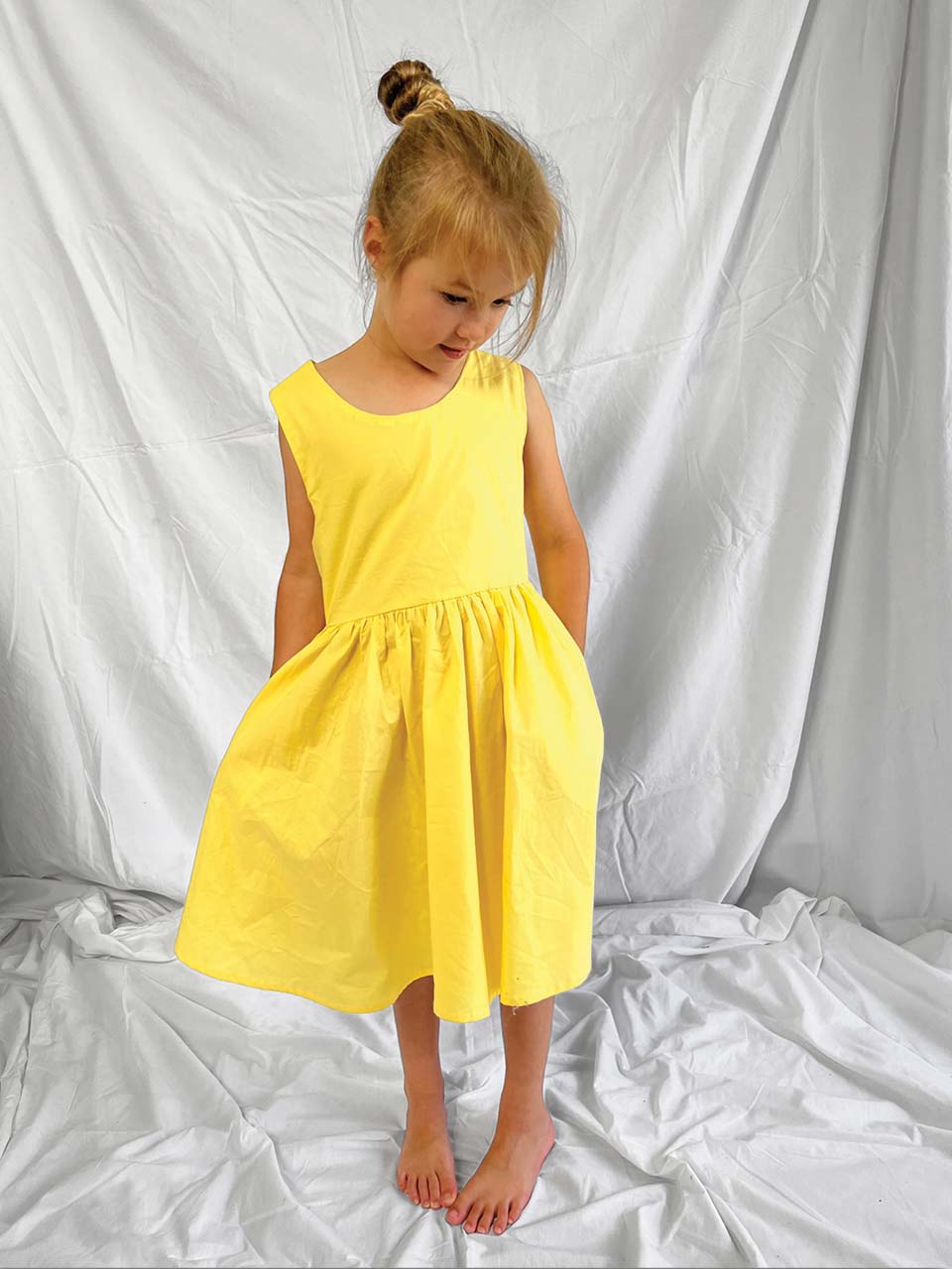 Yellow pinafore dress worn by a young girl with a white background