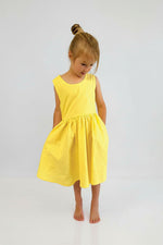 Young girl wearing Yellow pinafore dress against a plain background