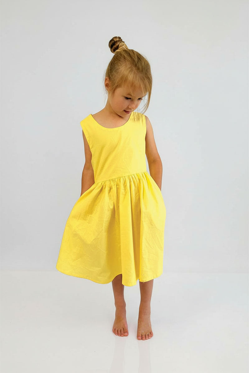 Young girl wearing Yellow pinafore dress against a plain background