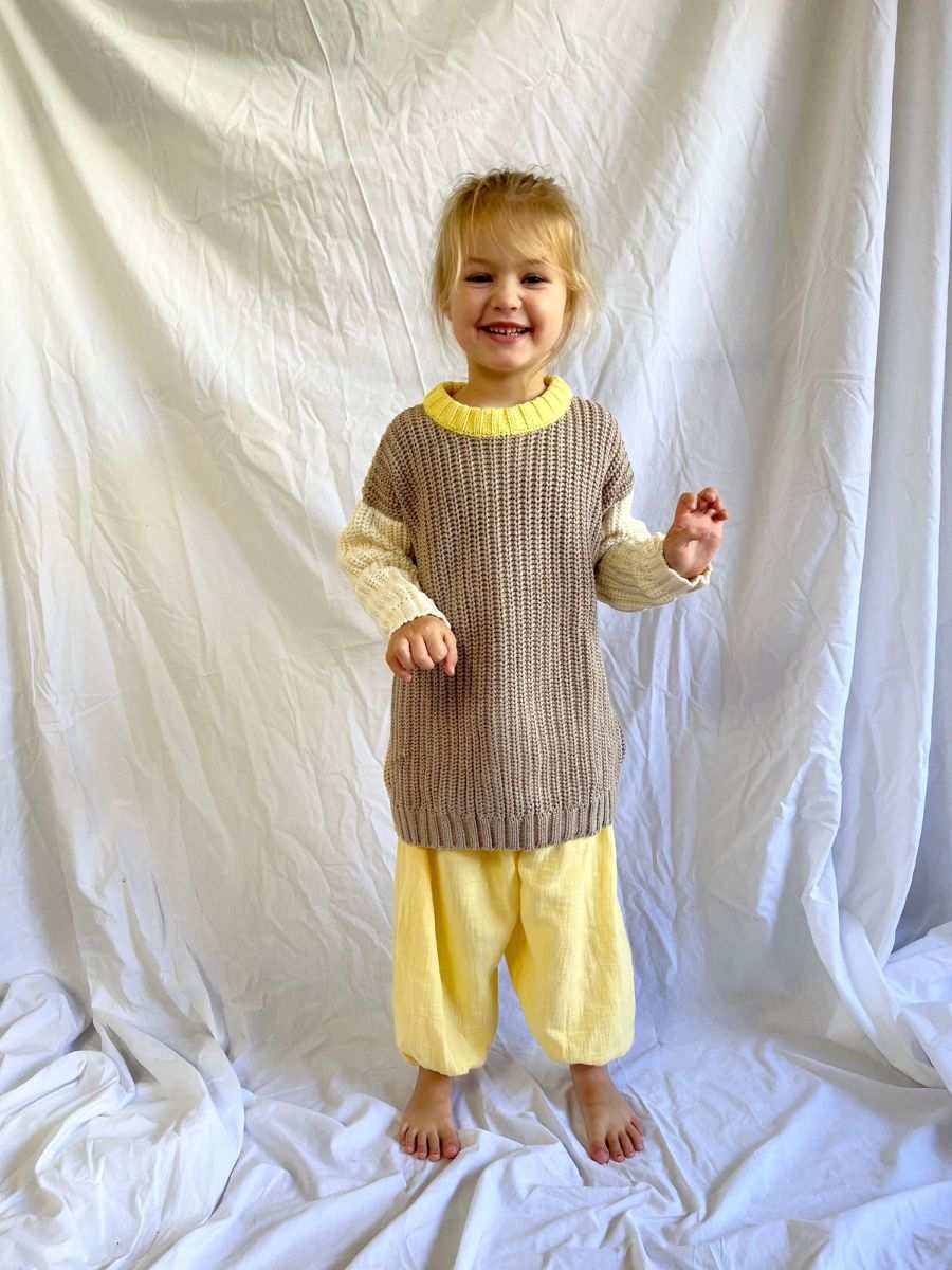 Young girl stood up smiling wearing our Anytime Knit in Desert colour