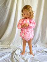 Young child playing with her hands while wearing a Long Sleeve Romper in Paisley Red colour