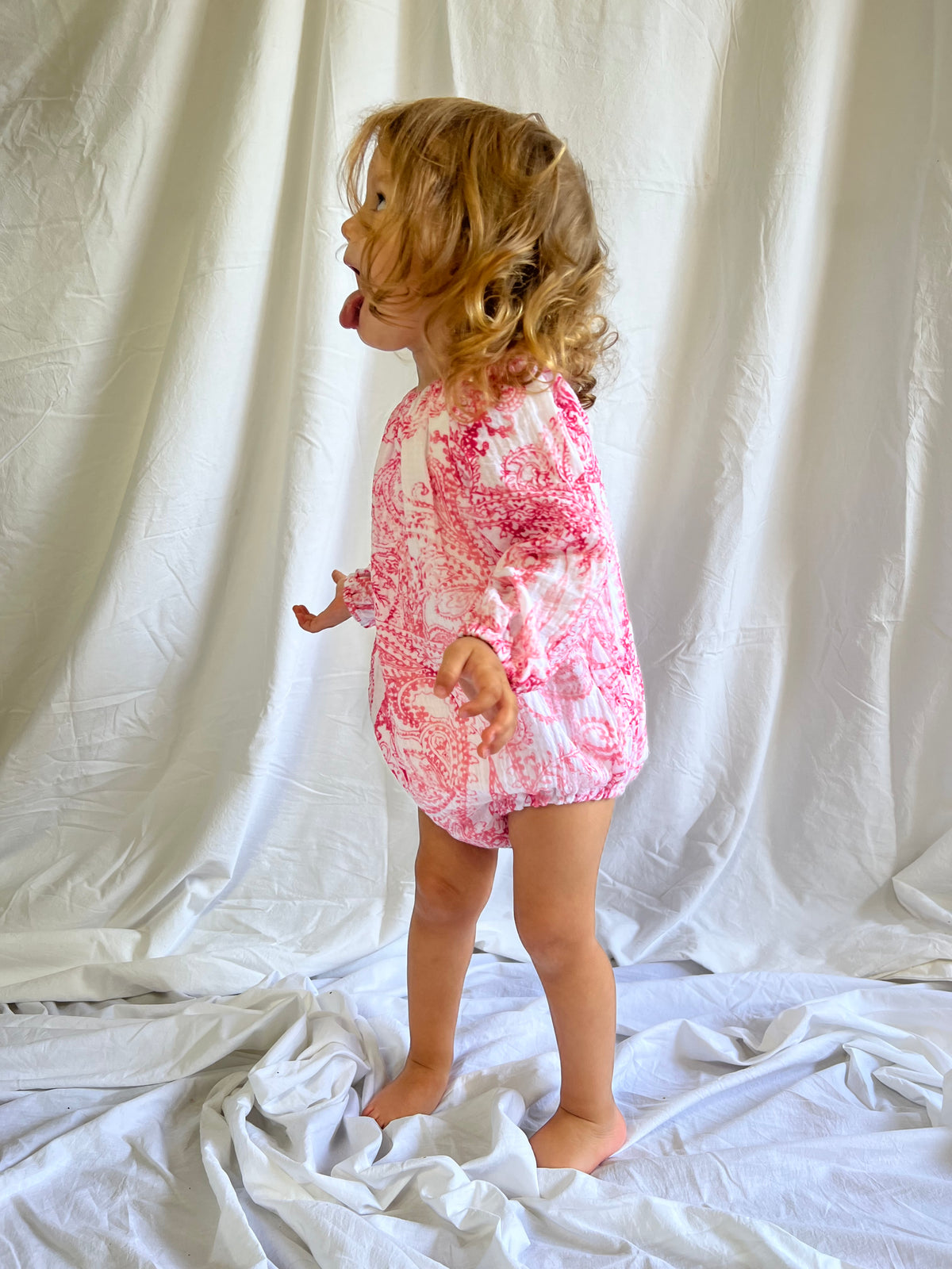 Young child poking her tongue out while wearing a Long Sleeve Romper in Paisley Red colour