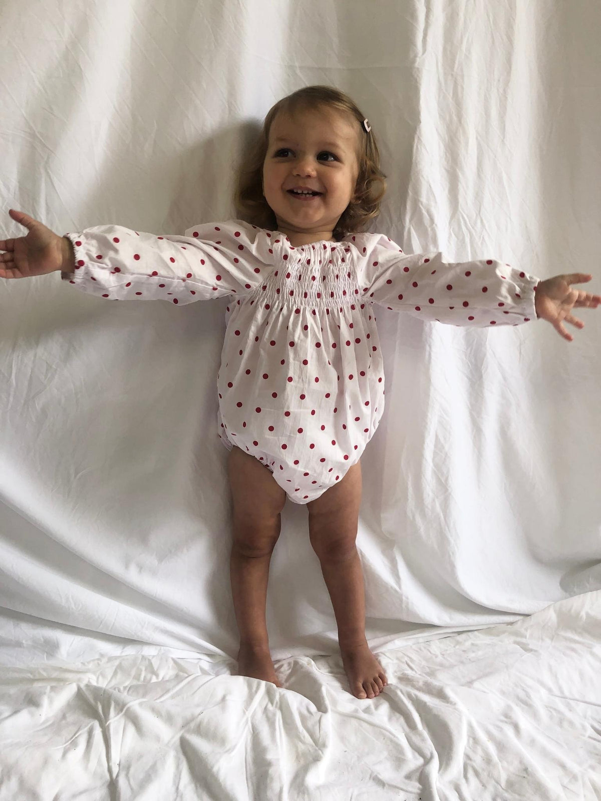 Romper smocked with long sleeves in red polka dot modelled front view