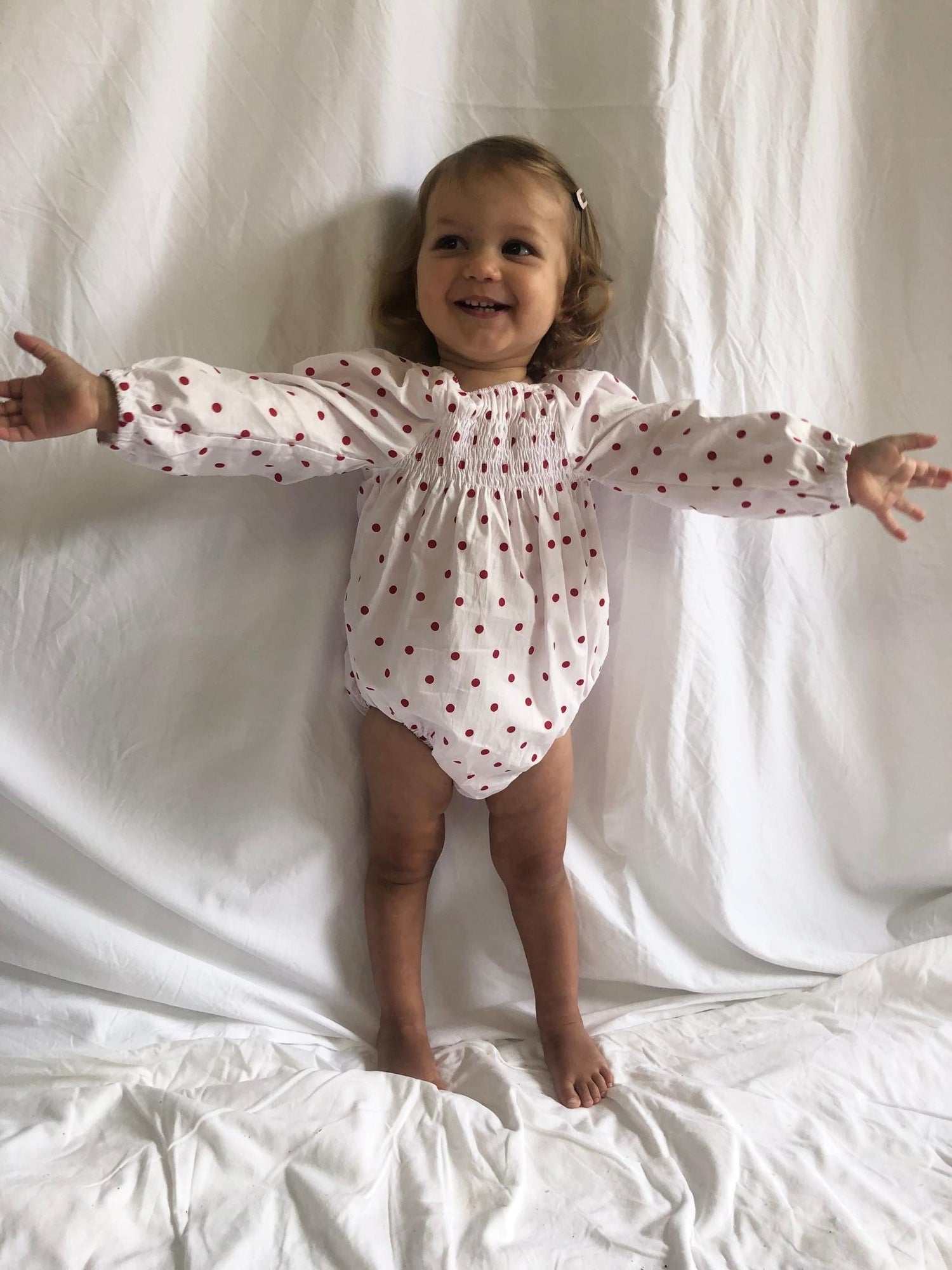 Romper smocked with long sleeves in red polka dot modelled front view